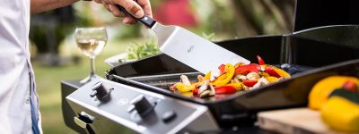 Gros plan sur une plancha d'une personne en train de cuire des poivrons en les remuants avec une spatule.