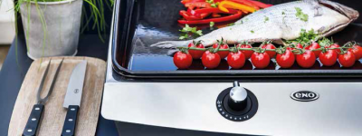 Zoom sur une plancha en train de cuire du poisson et des légumes.