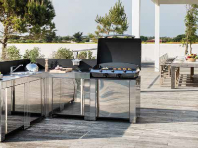 Cuisine extérieure en inox avec terrasse en bois et table extérieure.